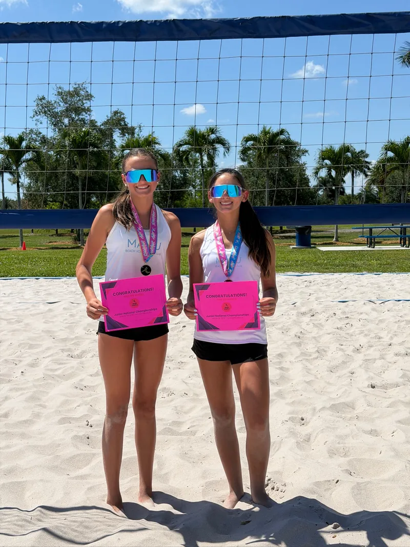 Two Mamu Beach athletes in club tanks wearing AVP Juniors medals and holding their 2026 national championship bid certificates